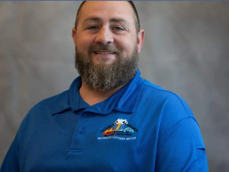 Bearded man smiling, wearing a blue polo shirt with a colorful embroidered logo.