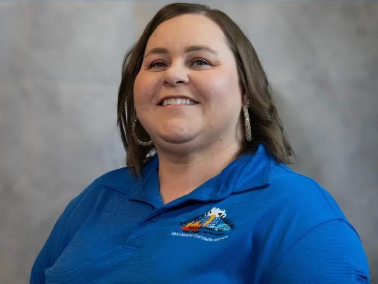 Smiling woman with shoulder-length brown hair wearing a blue polo shirt with a logo.