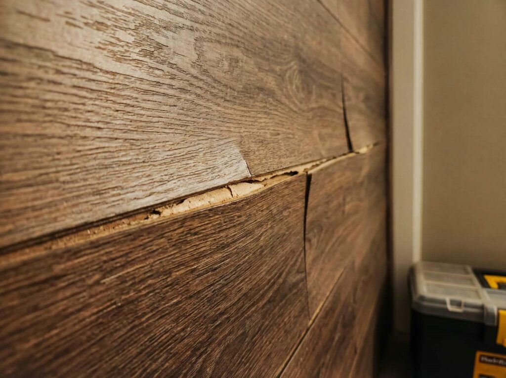 Close-up of cracked and damaged wooden wall panels with a toolbox in the background.