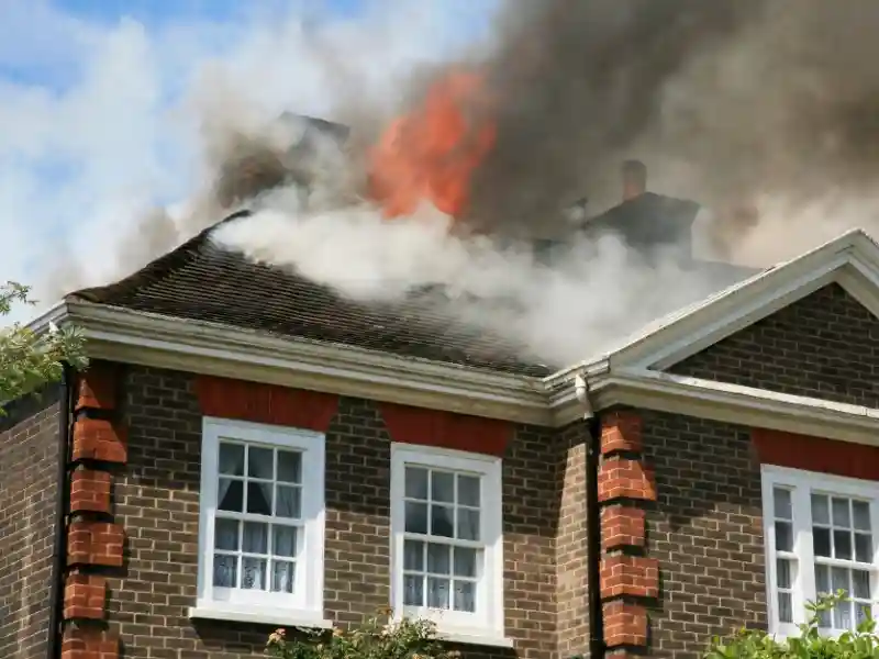 Flames and thick smoke rising from the roof of a brick house. water damage restoration in north alabama