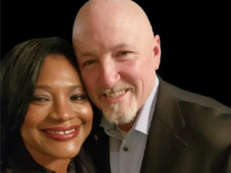 A smiling couple posing closely against a black background.
